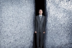 Businessman Being Squeezed By Two Large Granite Rocks
